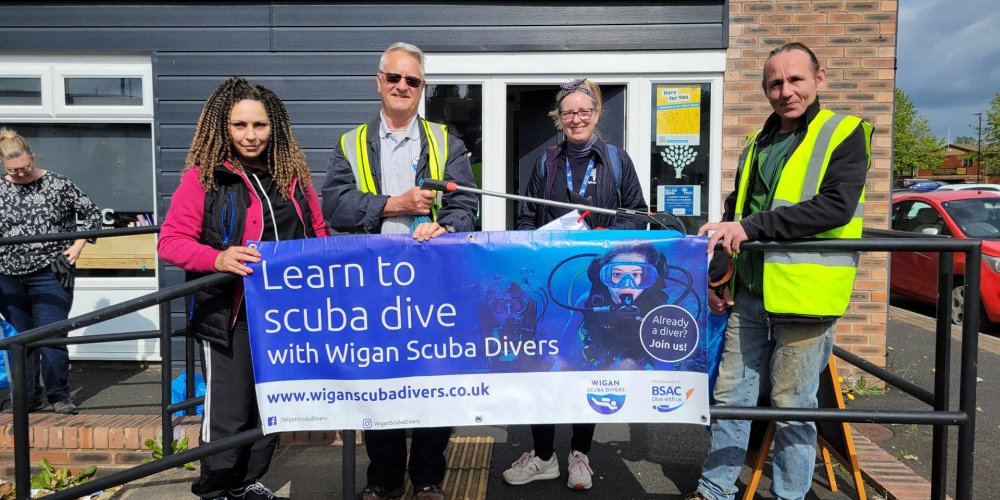 A picture of a few of our members posing in front of the Wigan and Leigh Carers venue, holding the Wigan Scuba Divers promotional banner